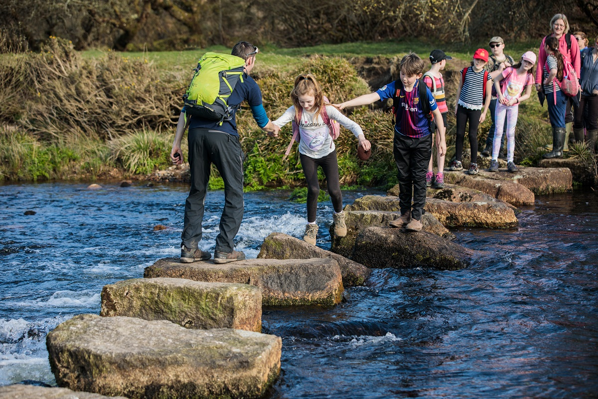 Children and an adult crossing river using steppingstones